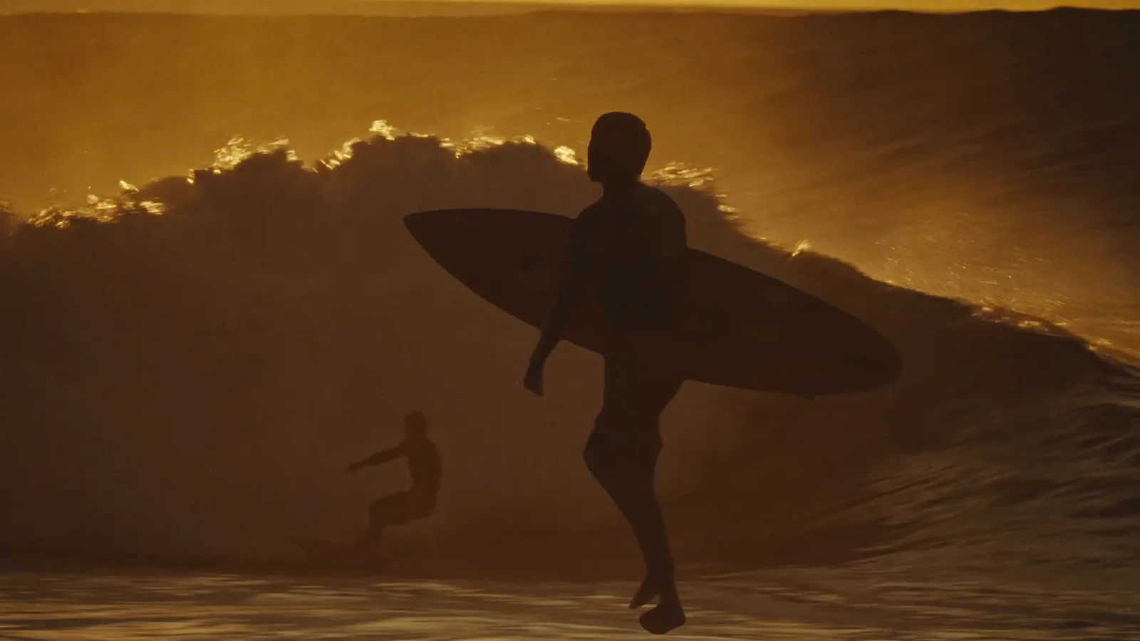 A surfer silhouetted against a golden wave at sunset