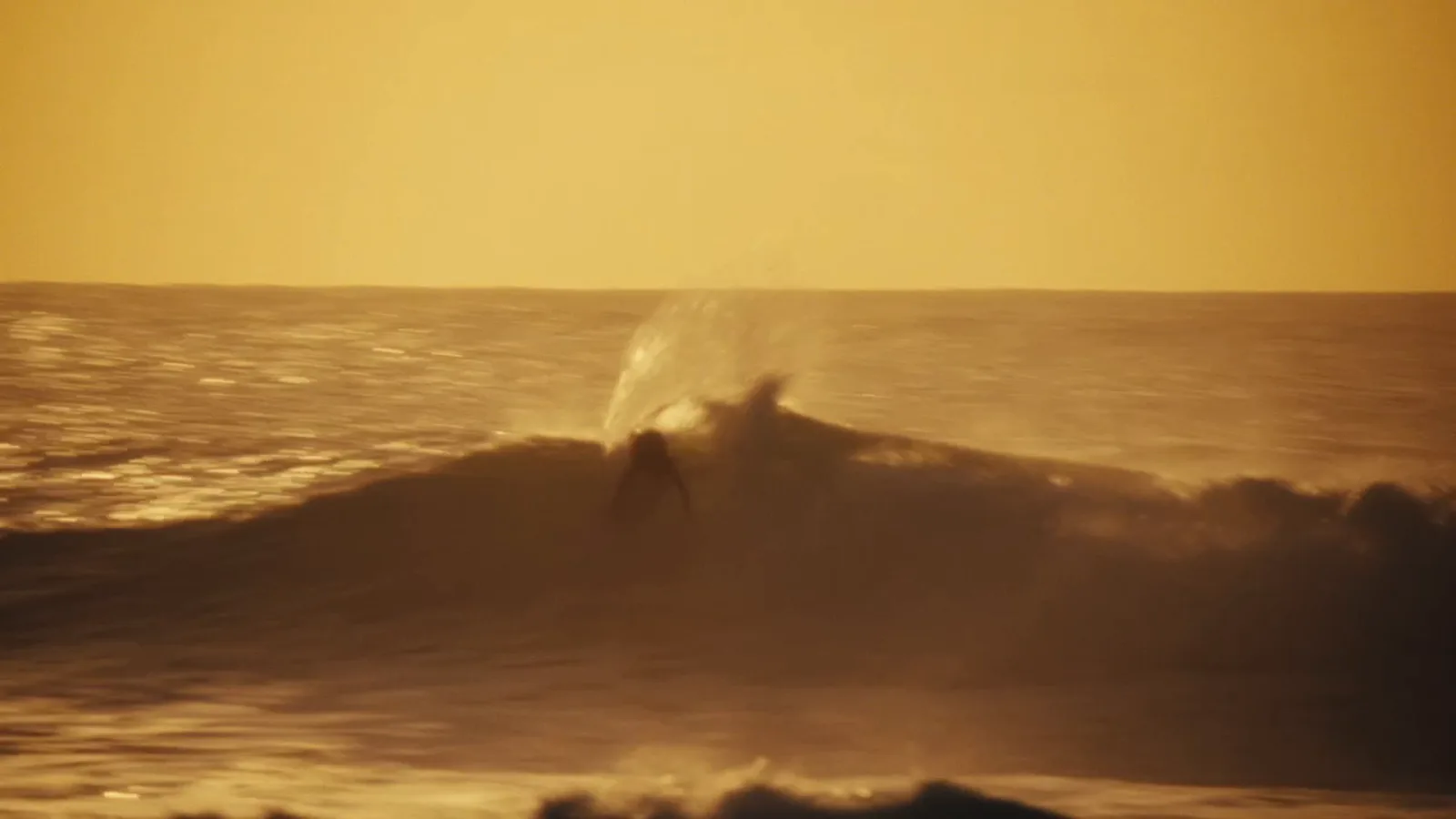A surfer riding a golden wave at sunset